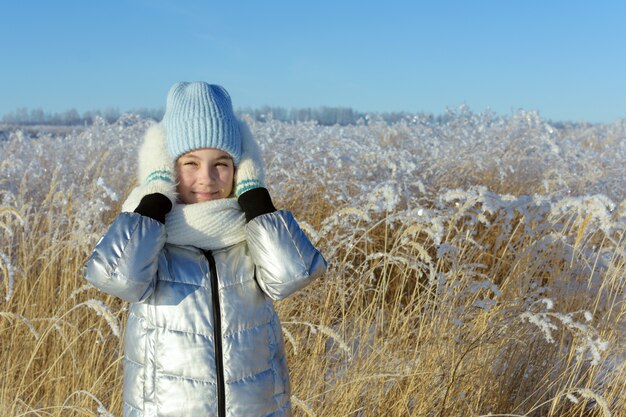 Ritratto di inverno della ragazza teenager sveglia che guarda l'obbiettivo e sorridente sul fondo dell'erba coperto di brina.