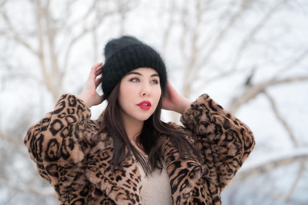 Winter portrait of female with long hair and red lips in fur coat with leopard pattern and black hat