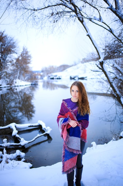 Winter portrait of a girl against the background of a frozen lake and trees with snow