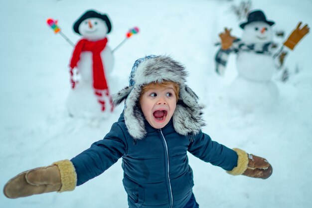 雪だるまを作る雪の庭の小さな男の子の冬の肖像画。雪だるまと遊ぶ子供