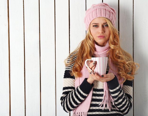 暖かい飲み物のカップと彼女のニットの暖かい服装で若い美しい金髪の女性の冬の肖像画
