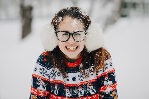 耳のマフ、雪に覆われた公園でポーズをとってセーターを着ている美しい少女の冬の肖像。探している女性