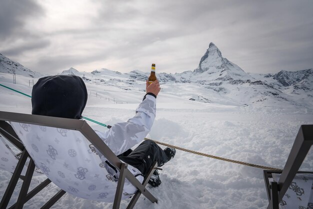 ゼルマットスキーリゾートでの冬のリラックスマッテールホーンに向かって雪の中でビールを楽しんでいる人