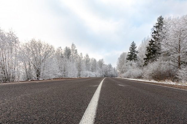 青い空と冷ややかな日の冬の道、雪に覆われた木々の風景、ストリップとアスファルトの上の氷を分割する白い高速道路のパターン