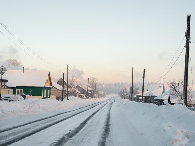 Фото Зимняя дорога через заснеженную деревню с сильным морозом и снежным туманом