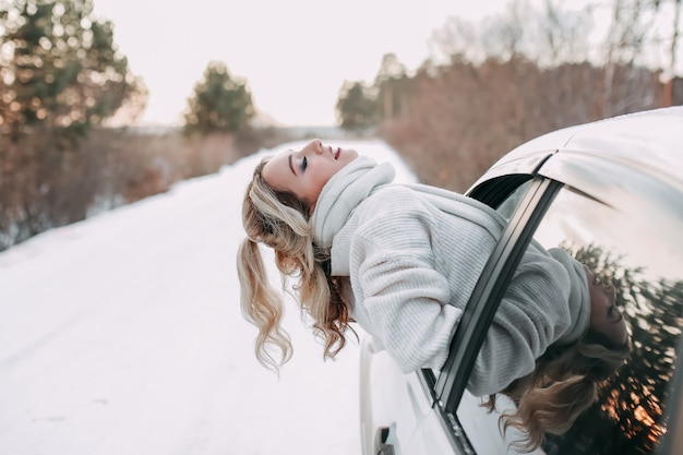 Photo winter road trip concept, happy traveling girl looking out of car window in nature