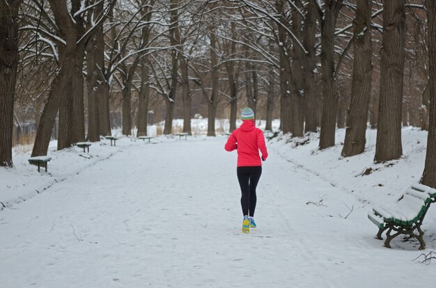 Winter running in park: happy active woman runner jogging in snow, outdoor sport and fitness concept