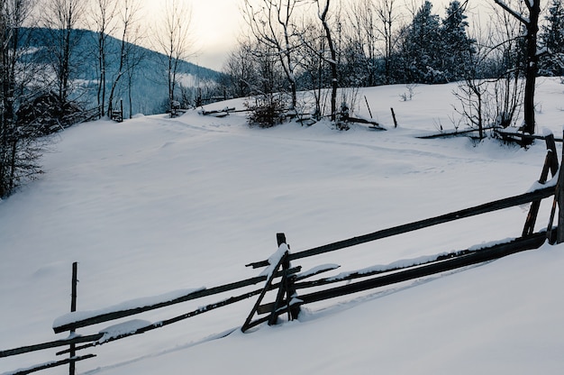 写真 冬の田園風景の村や農場の雪をかぶった山々と夕日の背景の森