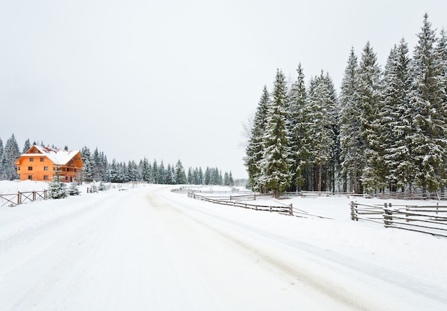 Winter saai berglandschap met hek, houten huis en landweg