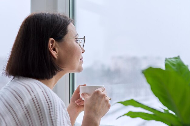 家の窓を見ている冬の雪の中年女性