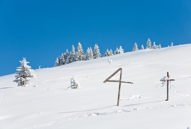 Winter snow covered fir trees on mountainside on blue sky background and wooden cross in front (Carpathians, Ukraine)