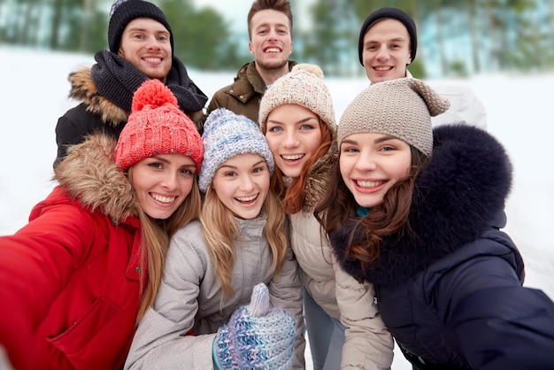 winter, technologie, vriendschap en mensenconcept - groep glimlachende mannen en vrouwen die selfie nemen en duimen buitenshuis tonen