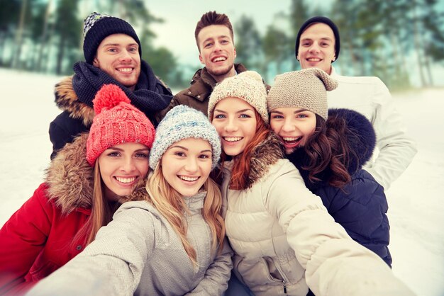 winter, technology, friendship and people concept - group of smiling men and women taking selfie outdoors