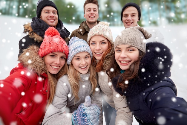 冬、テクノロジー、友情、人々のコンセプト-笑顔の男性と女性が自分撮りをして屋外で親指を立てるグループ