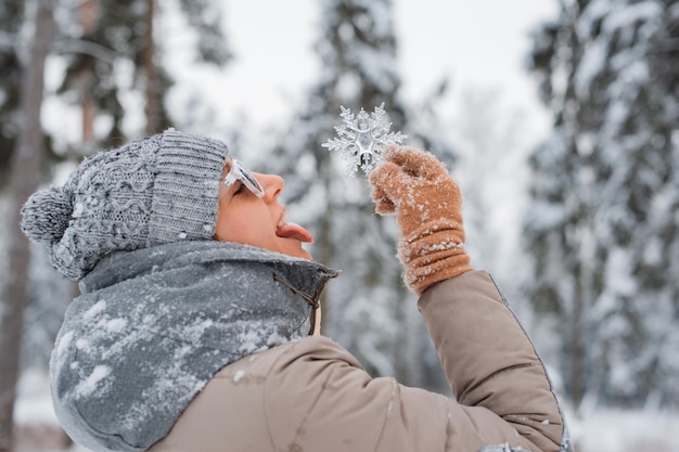 Orario invernale donna vestita di grigio alla moda indossando occhiali da sole lancia divertendosi a catturare i fiocchi di neve...