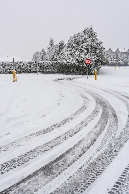 雪道の曲がり角に冬用タイヤの痕跡があり、前に一時停止の標識が付いています