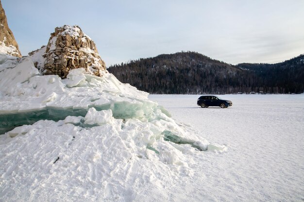 Winter travel Frozen river ice and rocks on the shore car and mountains in the background