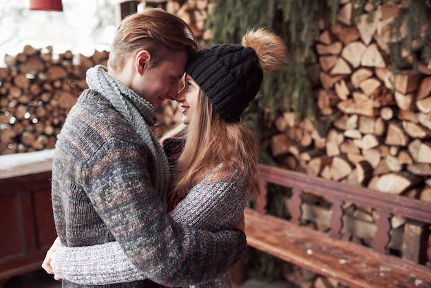 Зима, каникулы, пара, Рождество и люди - улыбающиеся мужчина и женщина в шляпах и шарфе, обнимающие деревянный загородный дом и снег