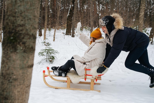 Winter vakantie. Een stel in een bos heeft plezier op een vrije dag, man duwt slee met zijn vrouw.