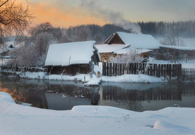 зимний деревенский пейзаж, дома у реки с дымящимися трубами, собака в сельском дворе