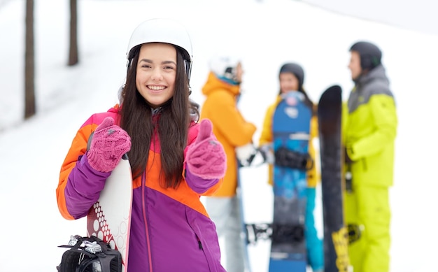 winter, vrije tijd, extreme sport, vriendschap en mensenconcept - gelukkige jonge vrouw in helm met snowboard en groep vrienden die duimen opdagen