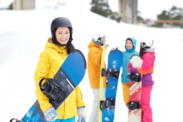 winter, vrije tijd, extreme sport, vriendschap en mensenconcept - gelukkige jonge vrouw in helm met snowboard en groep vrienden