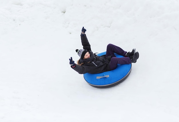 winter, vrije tijd, sport en mensen concept - gelukkige tiener of jonge man die op sneeuwbuis glijdt en overwinningsgebaar toont