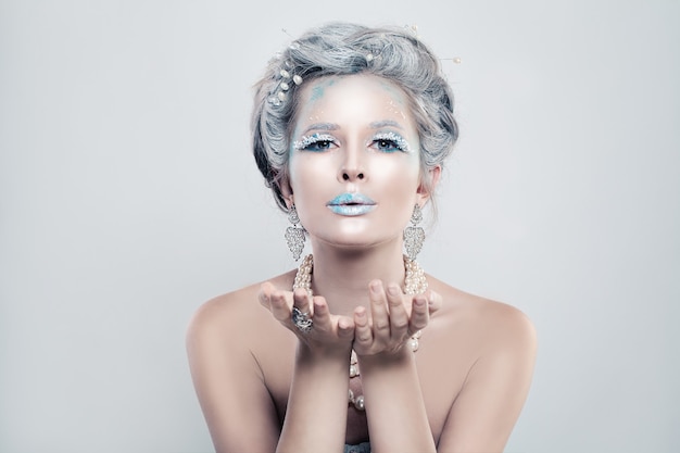 Winter vrouw mannequin met sneeuw glitters make-up blaast een kus