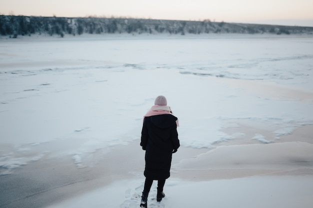 Winter walk. Woman walking out on frozen river background in cold time.