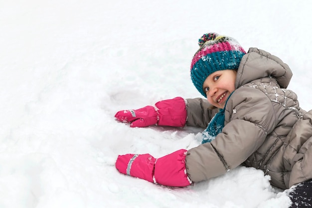 冬のウォーキングアクティビティ女の子は雪の中で横たわっていて、冬のスーツで子供を遊んでいます