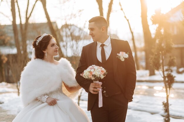 結婚式の日に雪に覆われた冬の公園で 抱きしめ合って笑顔で歩く幸せなカップル 雪の冬の天気で美しいカップルの冬のラブストーリー