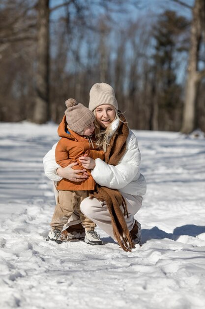 Fine settimana invernale madre e due figli in vestiti invernali caldi che si divertono a camminare nella foresta invernale tra gli alberi