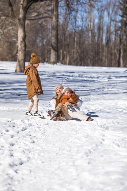 Foto fine settimana invernale madre e due figli in vestiti invernali caldi che si divertono a camminare nella foresta invernale tra gli alberi