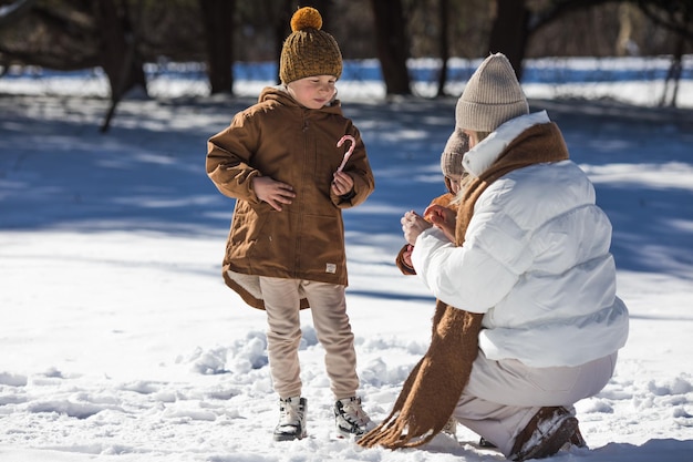 Winter weekend Mother and two sons in warm winterwear walking while having fun in winter forest among trees