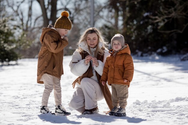 Winter weekend Mother and two sons in warm winterwear walking while having fun in winter forest among trees