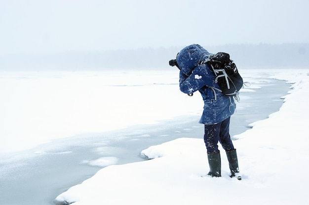 Winter white landscape of a frozen bay with melted ice, the photographer stands at the edge of the coast and takes pictures.