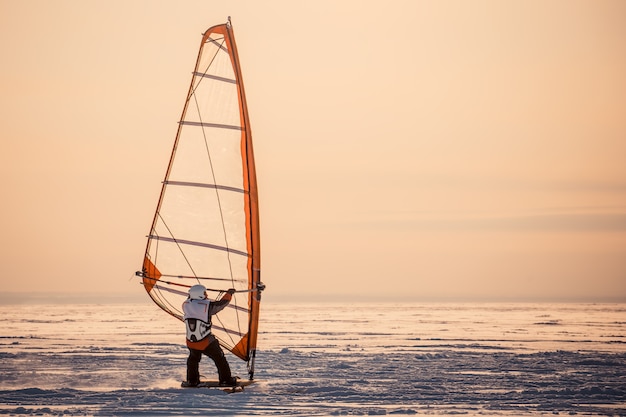 Winter windsurfing. Man riding a surf in the snow at sunset. Extreme winter sport. The rear view