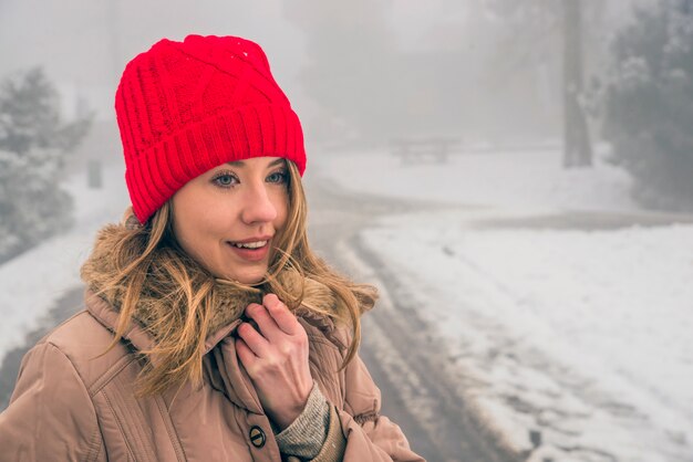 冬の女性は、幸せを探して、寒い冬の日には雪の中で笑顔で笑顔。暖かい帽子とジャケットで笑顔の若い女性の肖像画