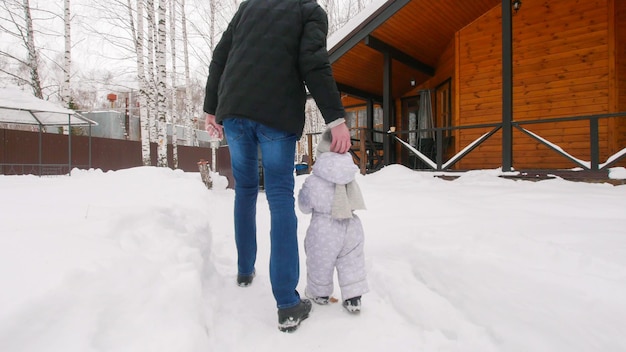 雪の中庭で赤ちゃんと一緒に歩く冬の若い家族