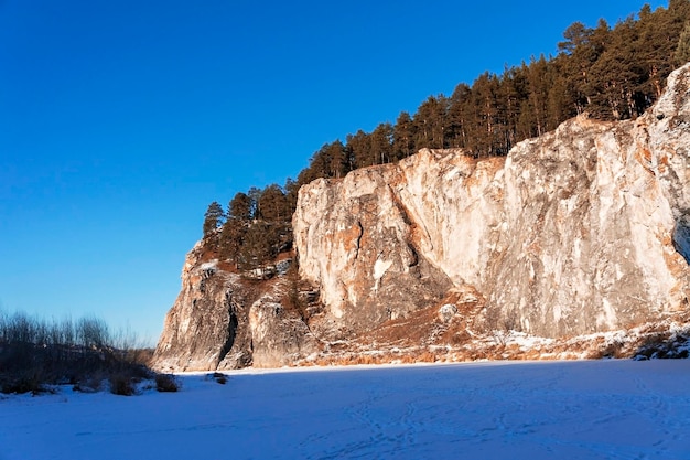 Winterberglandschap met kliffen op bevroren en besneeuwde rivier Rotsen met pijnbomen