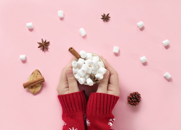 Winterdrank witte mok met marshmallows in vrouwelijke handen in gebreide kersttrui op roze