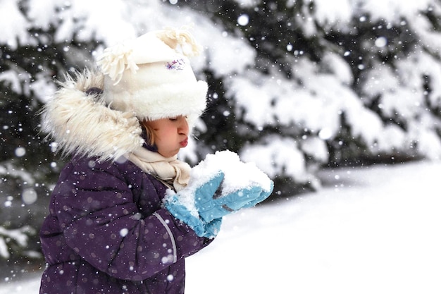 Winterkinderen lopen Kind blaast sneeuw in haar handen tijdens de wintersneeuwval