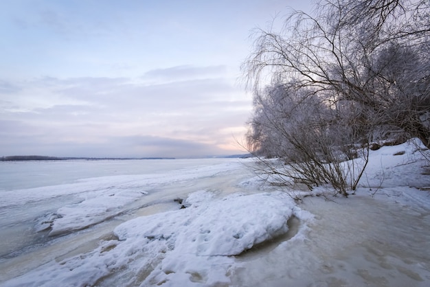 Winterlandschap bij zonsopgang, oever van een bevroren ijs.