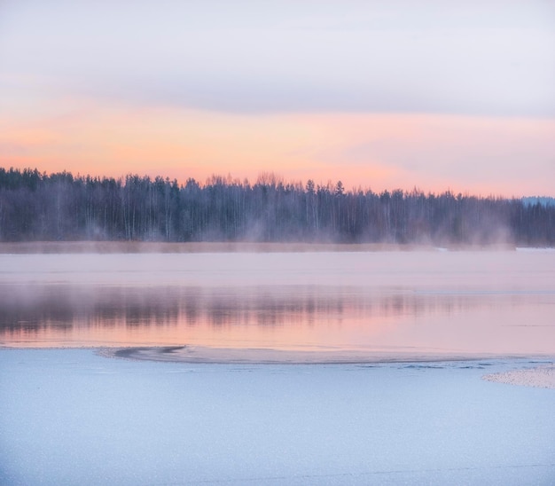 Winterlandschap, het water van het meer onder de sneeuw stijgt tegen de achtergrond van de dageraad en het bos.