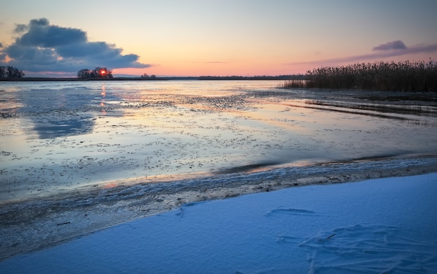 Winterlandschap met bevroren meer en avondrood. Kleurrijke oranje lucht