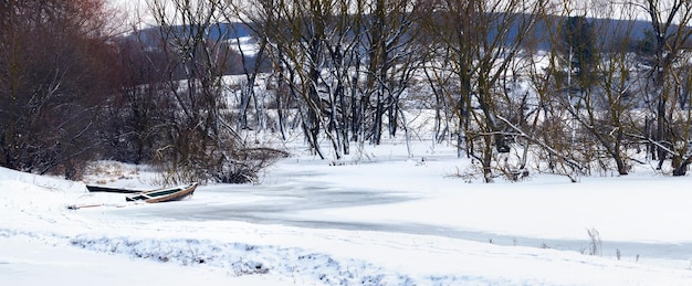 Winterlandschap met bomen en een boot bij een besneeuwde rivier