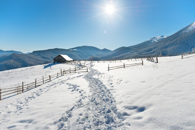 Winterlandschap met een oud landelijk huis op witte sneeuw met blauwe lucht en stralende zon