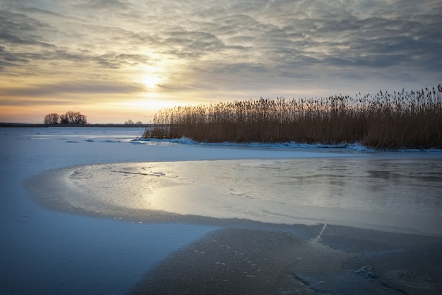 Winterlandschap met rivier, riet en avondrood. Samenstelling van de natuur.