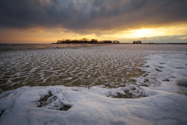 Winterlandschap met rivier, riet en bewolkte avondrood. Samenstelling van de natuur.