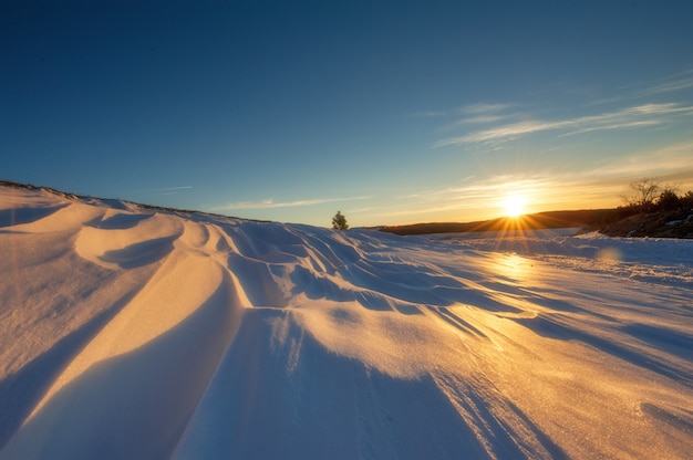 Winterlandschap met sneeuw bedekte velden en wegen in zonlichtstralen op de zonsondergang